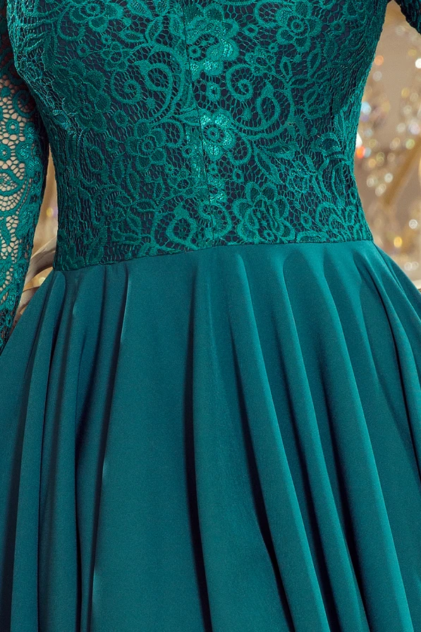 Elegantiška žalia suknelė su nėrinių viršumi ir ilgomis rankovėmis suteikia rafinuotumo ir moteriškumo. Plisuotas sijonas prideda žavesio ir elegancijos kiekvienam žingsniui.