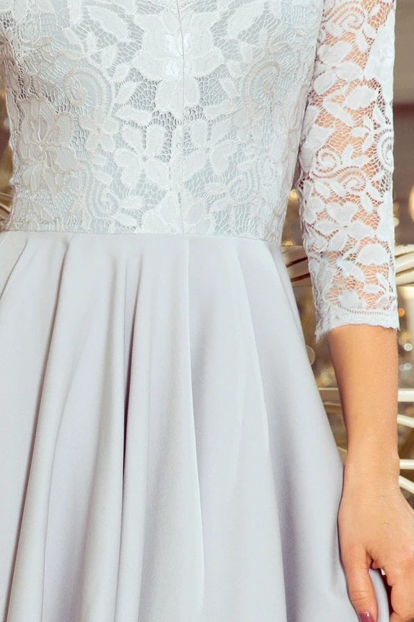 Elegantiška suknelė su nėriniuota viršutine dalimi ir trijų ketvirčių rankovėmis. Šviesiai pilkas sijonas suteikia subtilumo ir elegancijos.