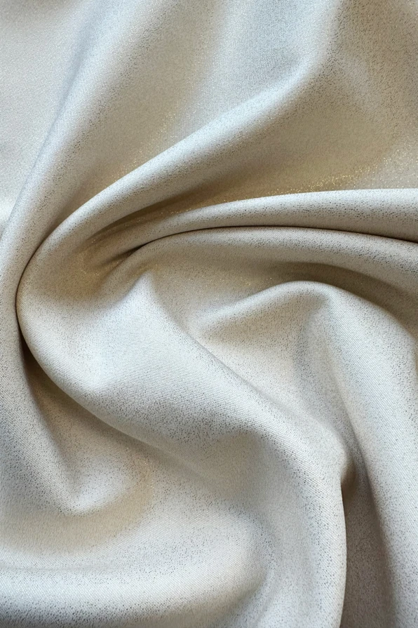 Elegantiška, smėlio spalvos suknelė su subtiliu blizgesiu, pagaminta iš aukštos kokybės audinio. Suknelė turi trapecijos formą, kuri suteikia elegancijos ir patogumo.
