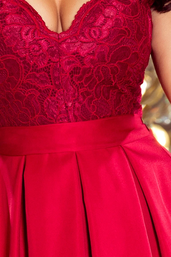 Elegantiška raudona suknelė su gilia iškirpte ir nėriniuotu viršumi suteikia prabangos ir moteriškumo įspūdį. Plisuotas sijonas pabrėžia figūrą ir suteikia elegancijos.