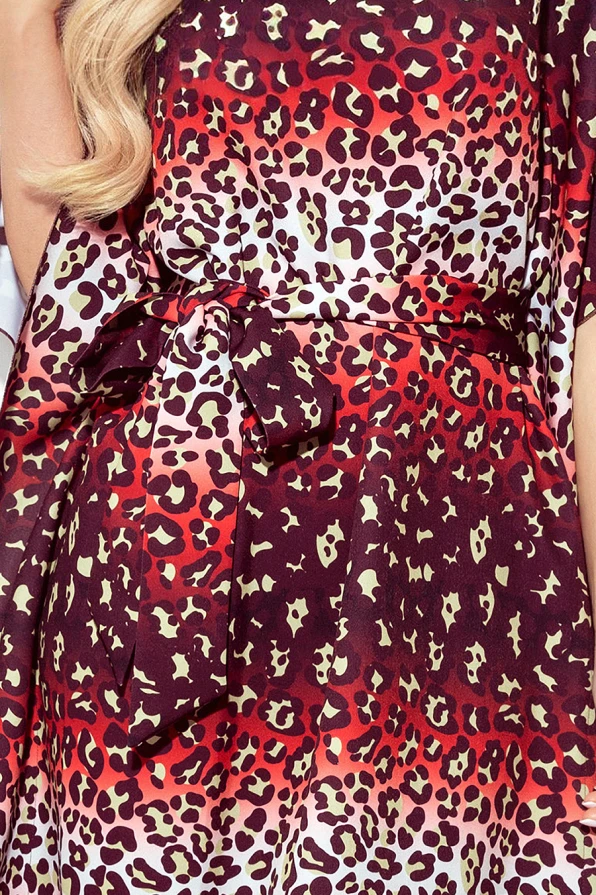 Moteriška suknelė su ryškiu leopardiniu raštu, kuris pereina nuo raudonos iki smėlio spalvos. Suknelė turi elegantišką diržą, kuris pabrėžia liemenį.