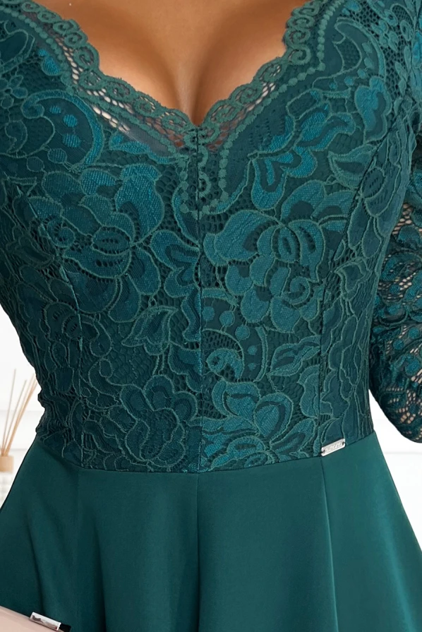 Elegantiška suknelė su žaliu nėriniuotu viršumi ir subtiliu gėlių raštu. Suknelė turi elegantišką iškirptę ir prigludusį siluetą, pabrėžiantį figūrą.