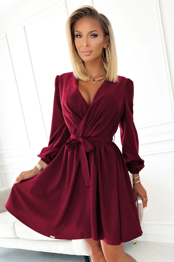 Elegantiška bordo spalvos suknelė su V formos iškirpte ir ilgomis rankovėmis, pabrėžianti moterišką siluetą. Suknelė turi juosmenį pabrėžiantį diržą, suteikiantį elegancijos ir rafinuotumo.