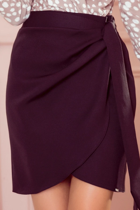Eleganti tamsiai violetinė sijonėlė su dekoratyviniu surišimu šone. Audinys švelniai priglunda prie kūno, suteikdamas rafinuotą ir moterišką išvaizdą.