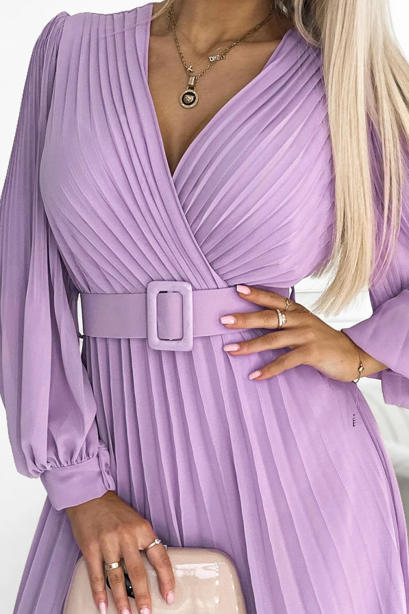 Šviesiai violetinė, plisuota suknelė su ilgomis rankovėmis ir elegantišku diržu pabrėžia moterišką siluetą. Suknelė turi subtilų V formos iškirpimą, suteikiantį rafinuotumo.