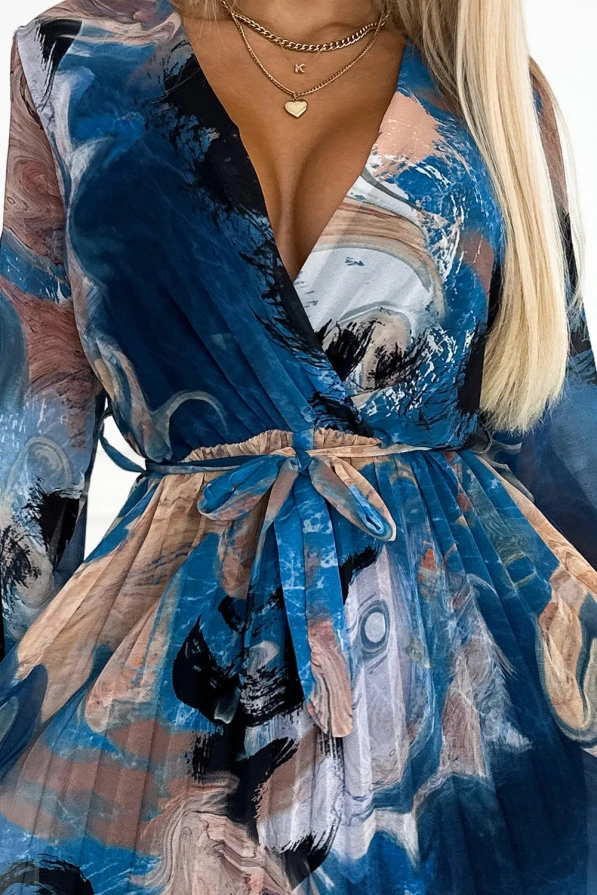 Mėlyna suknelė su abstrakčiu raštu ir plisuota sijono dalimi suteikia elegancijos ir modernumo. Suknelė turi V formos iškirptę ir yra sujuosta dirželiu, pabrėžiančiu liemenį.