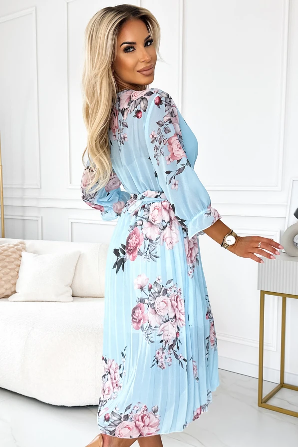 Mėlyna plisuota suknelė su gėlių raštu, suteikianti elegancijos ir lengvumo pojūtį. Suknelė turi ilgomis rankovėmis ir subtilų dirželį, pabrėžiantį liemenį.