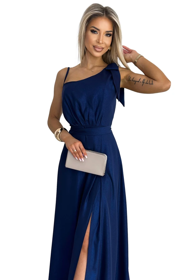 Ilga, blizganti suknelė su vienu petnešėliu ir elegantišku skeltuku priekyje. Suknelė yra tamsiai mėlynos spalvos, suteikianti rafinuotumo ir prabangos įspūdį.
